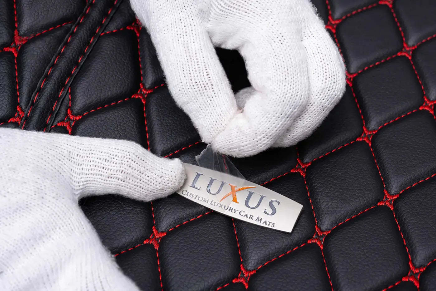Gloved hands revealing the Luxus seal of authenticity on a black mat with red diamond stitching